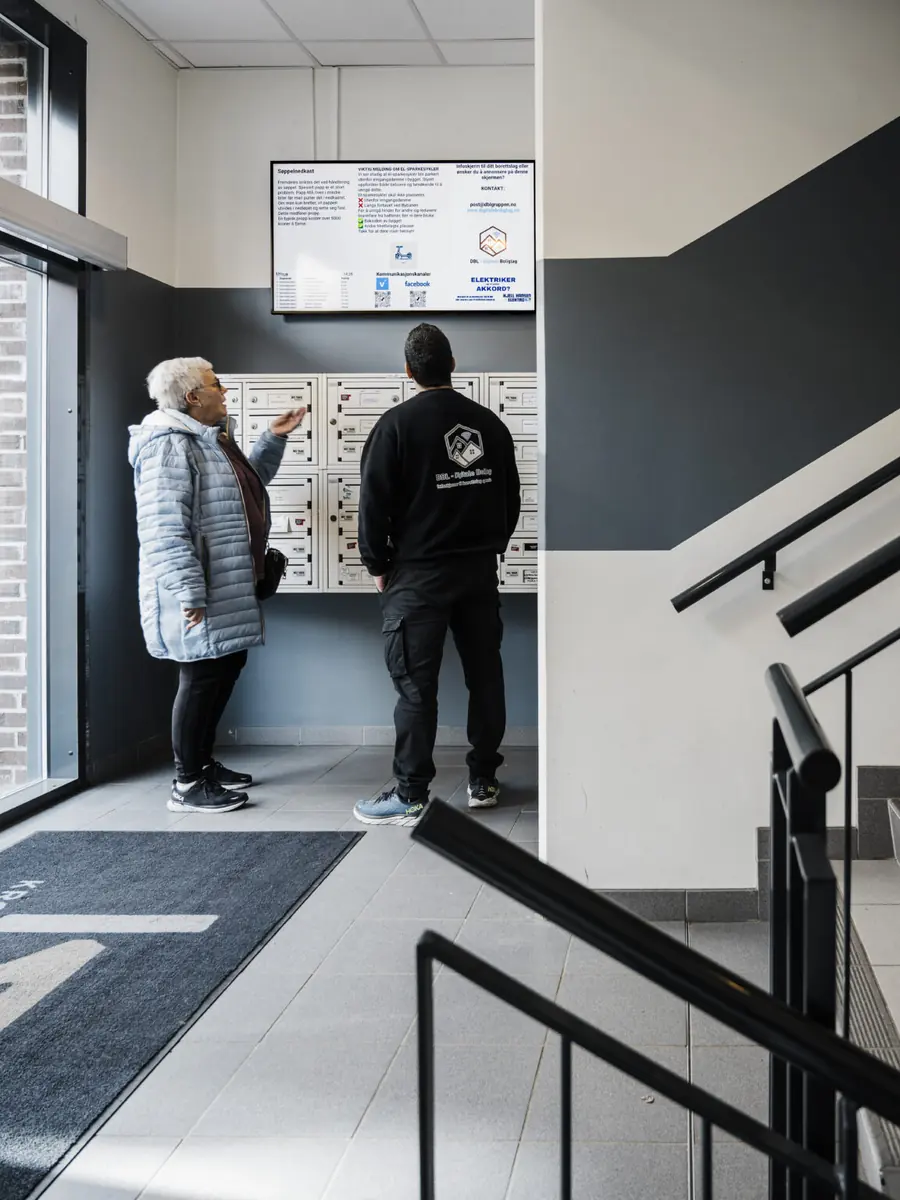 To beboere ser på infoskjermen ved postkassene i en lys oppgang