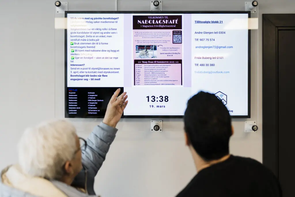 Beboer peker på en beskjed på infoskjermen i oppgangen